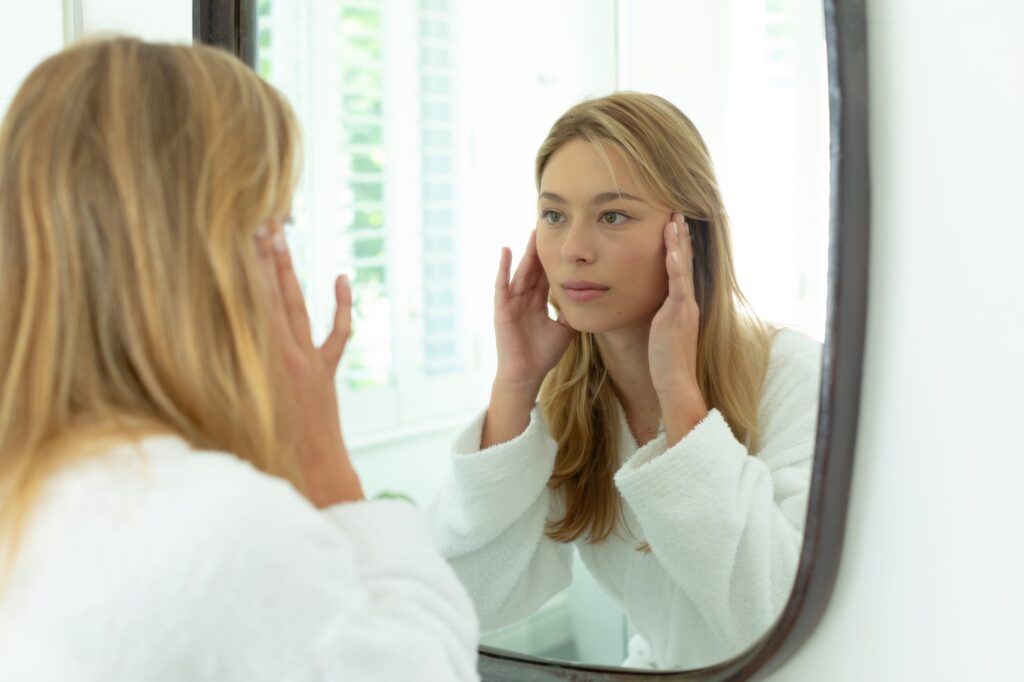 A woman sits in the bathroom and examines her results after learning how to reduce facial fat in Denville