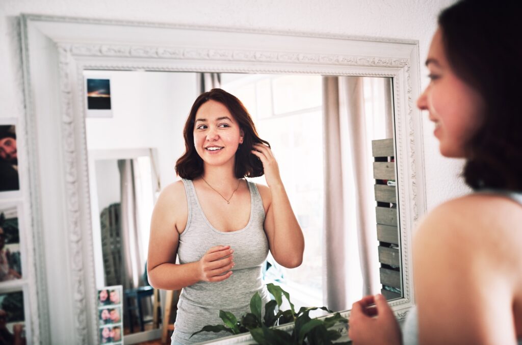 Woman looking at herself in the mirror smiling after hormone therapy for women in Denville