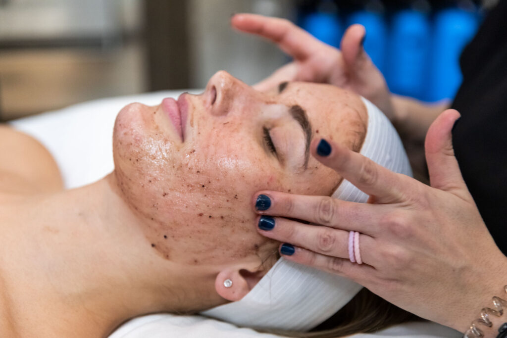 Woman with eyes closed as professional massage facial serum on her cheeks.