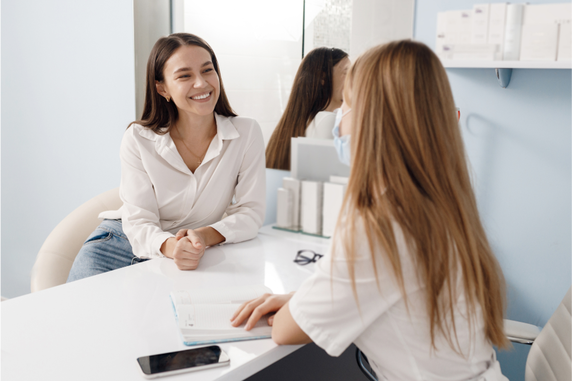 A blonde female patient smiling at a brunette provider at Exhibit Medical Aesthetics while they are discussing her treatment options for skin rejuvenation in Denville.