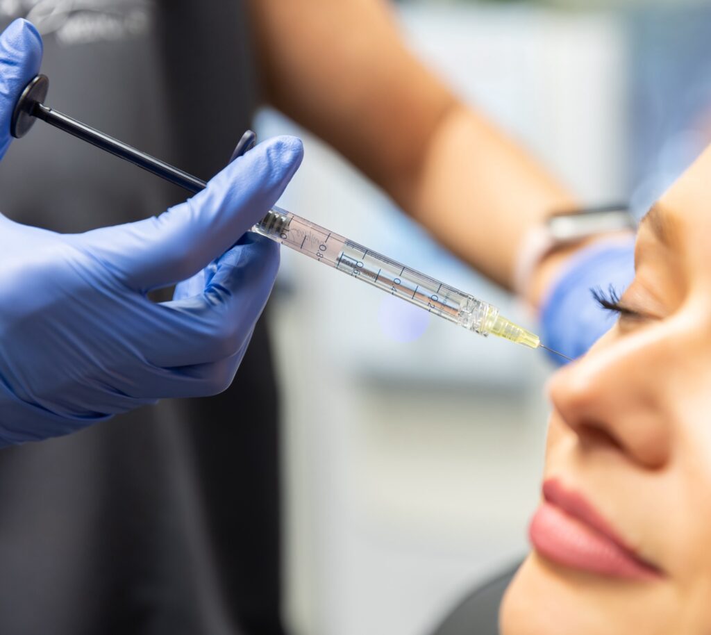Woman with eyes closed as nurse inserts needle into her cheek.