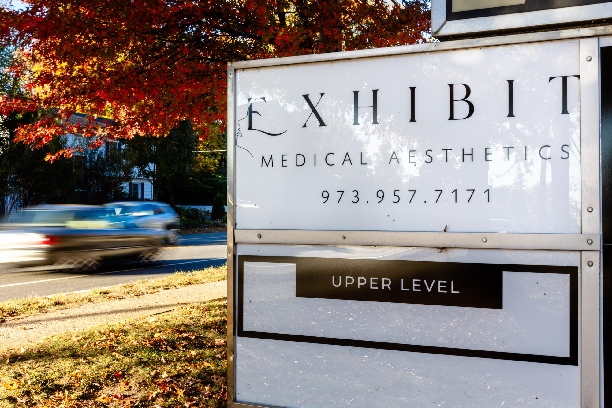 A close up of the outdoor sign for Exhibit Medical Aesthetics, where patients come from far away to receive hyperpigmentation treatment in Denville.|