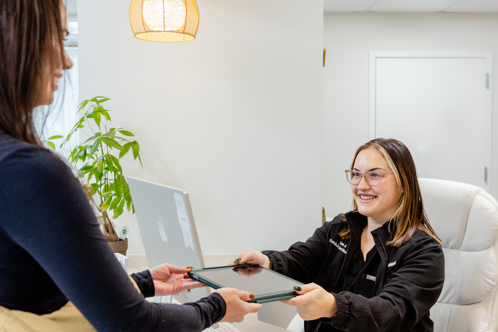 A female patient checking in at the Exhibit Medical Aesthetics front desk for brow lamination near Chatham, NJ.
