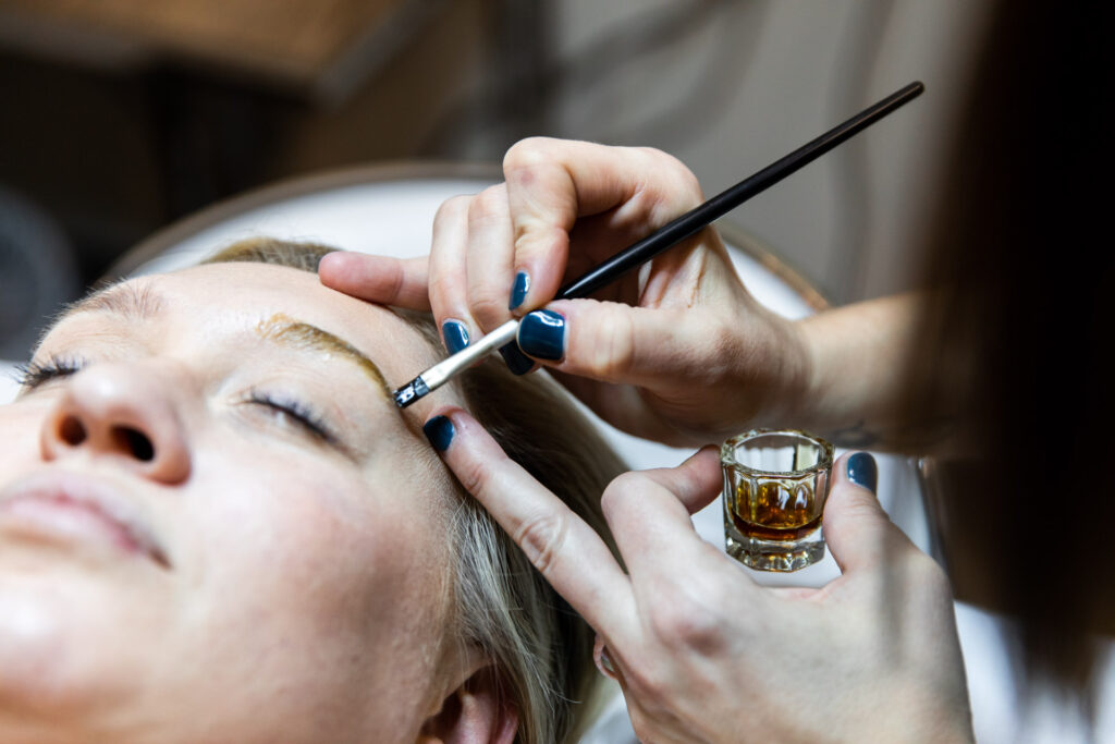 Woman with eyes closed lying down while practictoner applies eyebrow tint