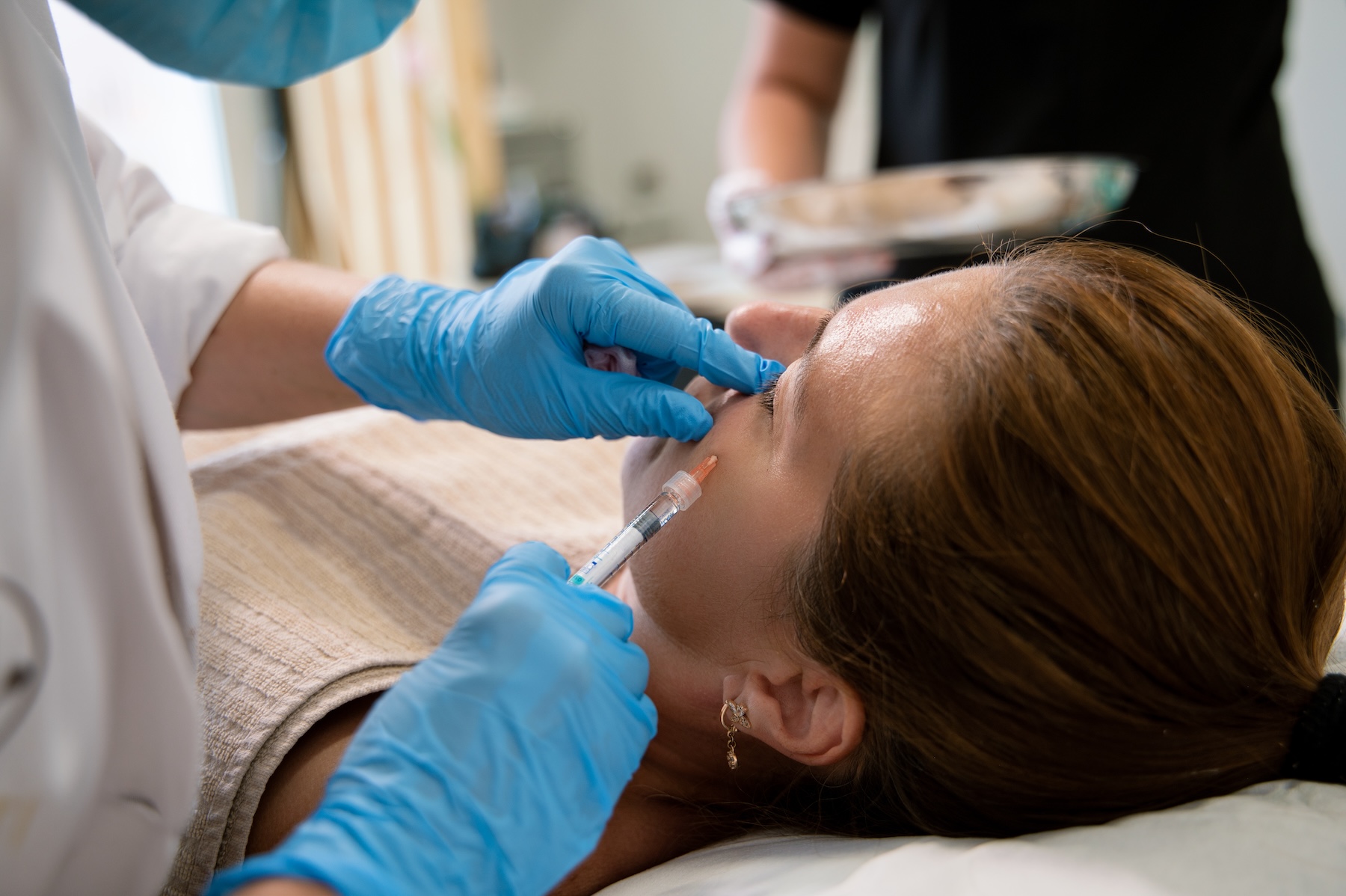 A brunette woman at Exhibit Medical Aesthetics laying down in a comfortable treatment chair while she receives injections of Skinvive near Chatham, NJ.