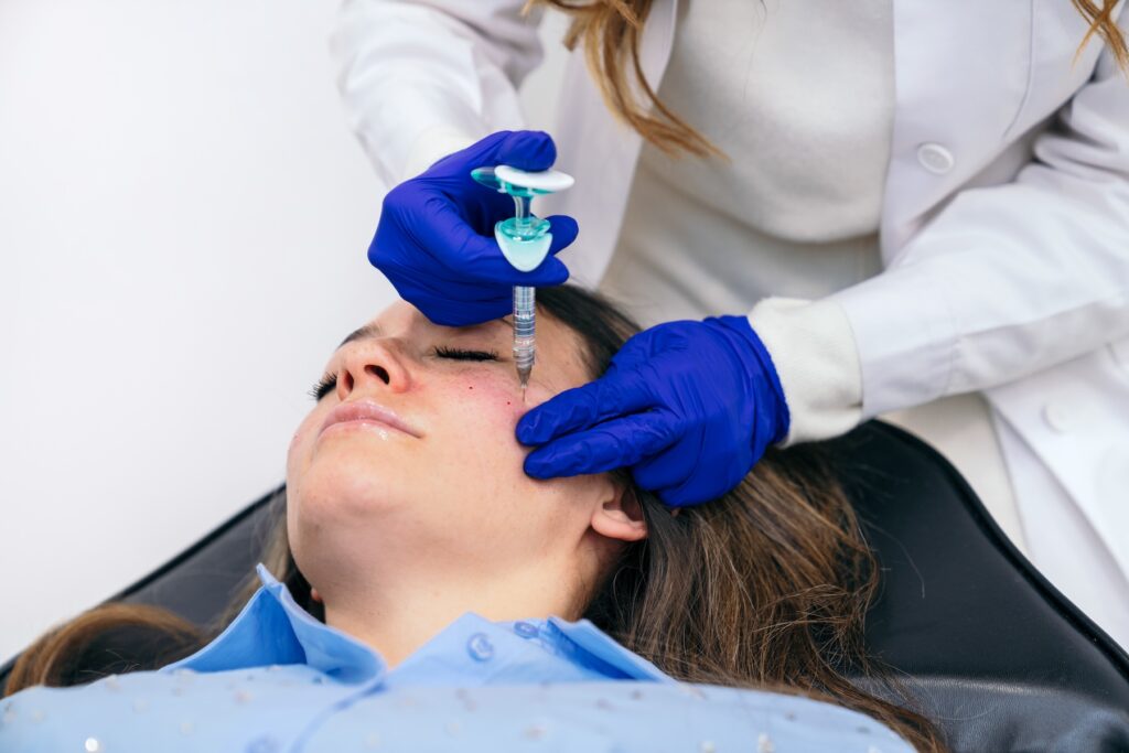 Medical professional in blue gloves injects needle into patient's face.