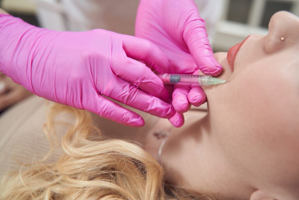 Photo of woman's lower face with nurse wearing gloves inserting needle next to her lips.