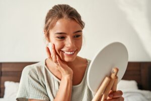 A young happy woman looks in the mirror during pregnancy-safe skin care in Denville.